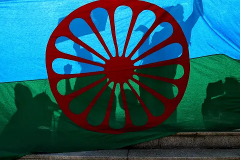 People cast shadows on the Roma flag during an anti-racism march by members of the Romanian Roma community celebrating the Romani Resistance Day in Bucharest, Romania, Saturday, May 18, 2019. On May 16, 1944 Roma prisoners in the Auschwitz concentration camp resisted an attempt by the Nazi troops to liquidate their camp, which postponed the action until August the same year. (AP Photo/Vadim Ghirda)